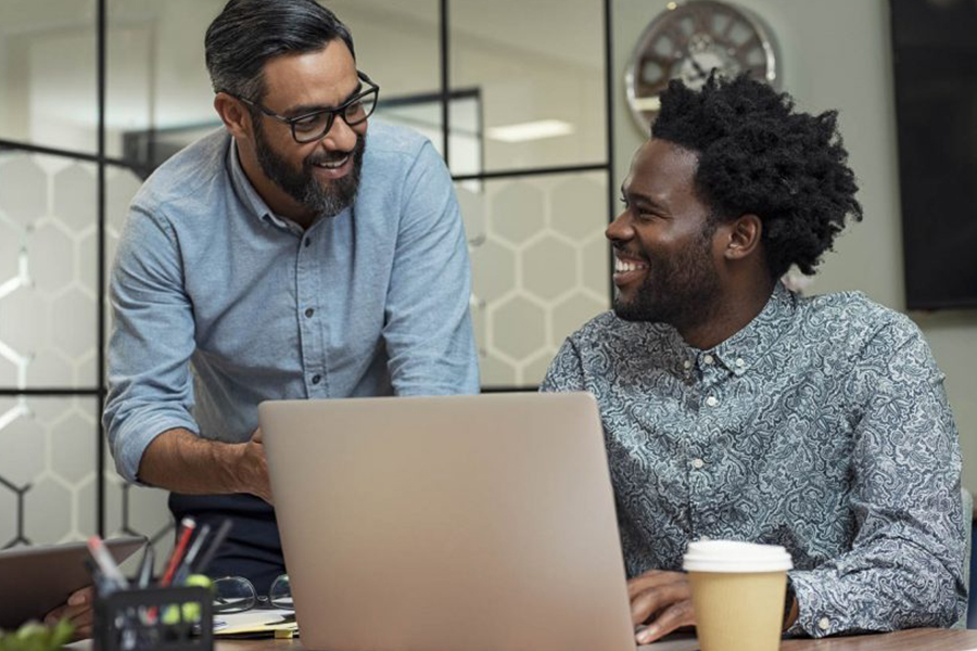 Two coworkers smiling and looking at a laptop together in a conference room